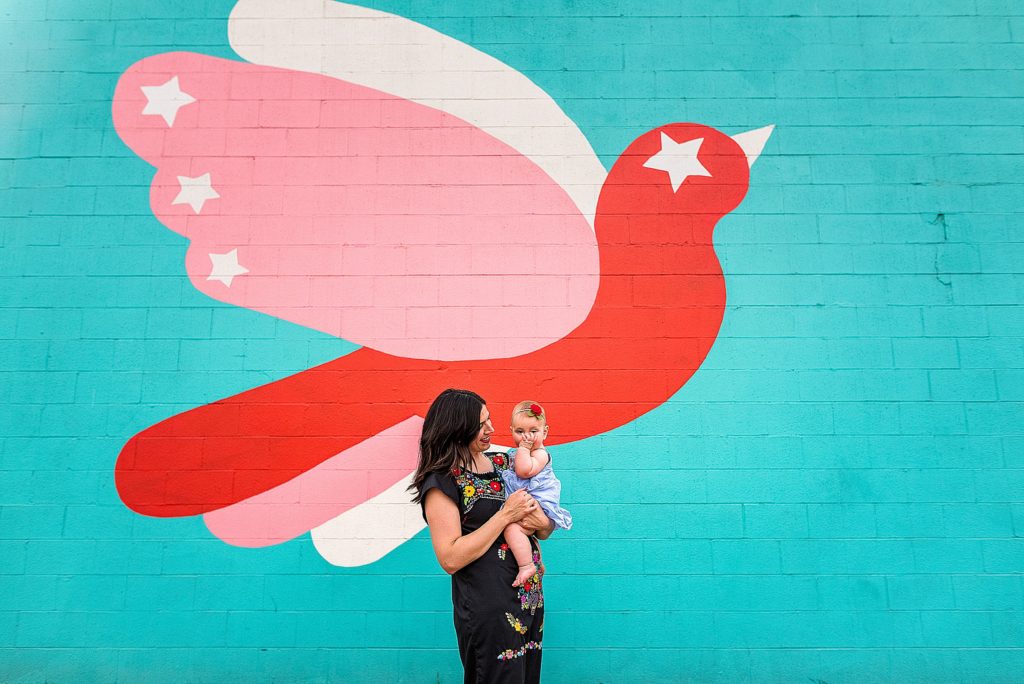 Charlotte Lifestyle Photographer also serving Mooresville, Davidson, Cornelius, Huntersville specializes in family, newborn, branding, etc Family sessions mom and baby by colorful mural of a bird teal pink red